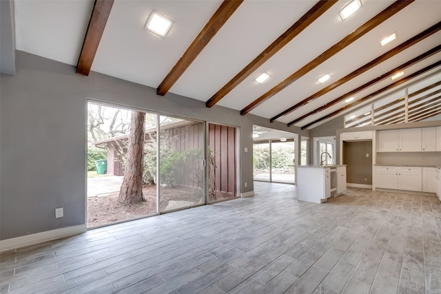 unfurnished living room with beamed ceiling, high vaulted ceiling, light hardwood / wood-style floors, and sink