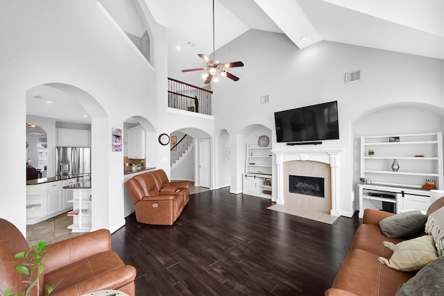 living room featuring built in features, high vaulted ceiling, a tiled fireplace, ceiling fan, and hardwood / wood-style flooring