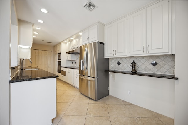 kitchen featuring light tile patterned flooring, dark stone countertops, decorative backsplash, white cabinetry, and stainless steel fridge