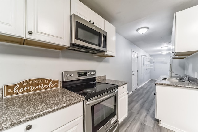 kitchen with stainless steel appliances, white cabinetry, a sink, and wood finished floors