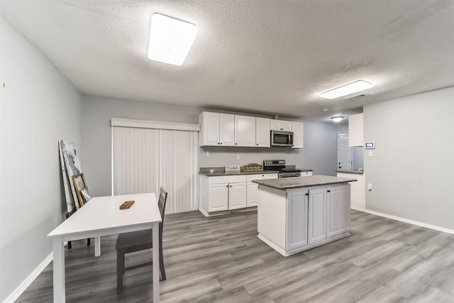 kitchen featuring a textured ceiling, wood finished floors, white cabinets, appliances with stainless steel finishes, and a center island