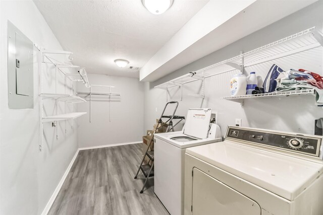 laundry room featuring washer and clothes dryer, light wood-type flooring, laundry area, electric panel, and baseboards