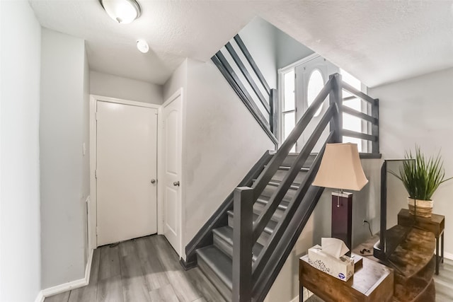 staircase featuring a textured ceiling, wood finished floors, and baseboards