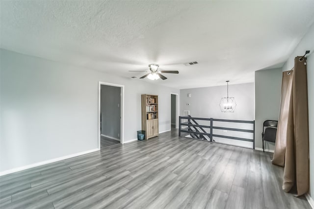 unfurnished room featuring baseboards, visible vents, wood finished floors, a textured ceiling, and ceiling fan with notable chandelier