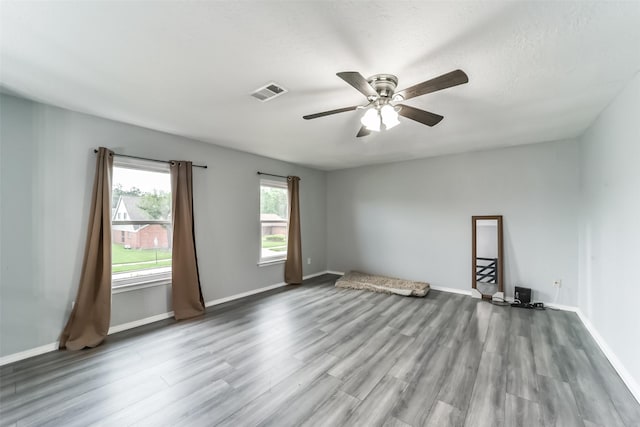 spare room with a ceiling fan, visible vents, baseboards, and wood finished floors