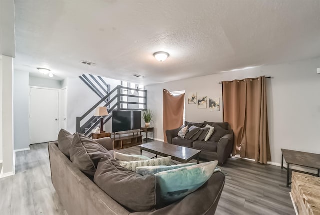 living area featuring baseboards, visible vents, wood finished floors, stairs, and a textured ceiling