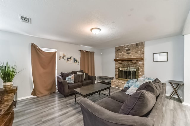 living room featuring a fireplace, visible vents, a textured ceiling, wood finished floors, and baseboards