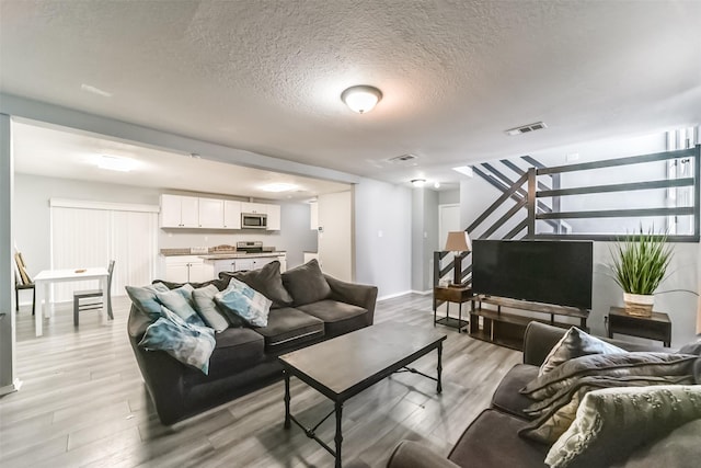 living room featuring a textured ceiling, light wood finished floors, stairs, and visible vents