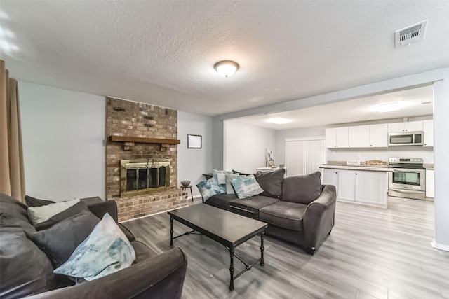 living room featuring visible vents, a fireplace, a textured ceiling, and light wood finished floors