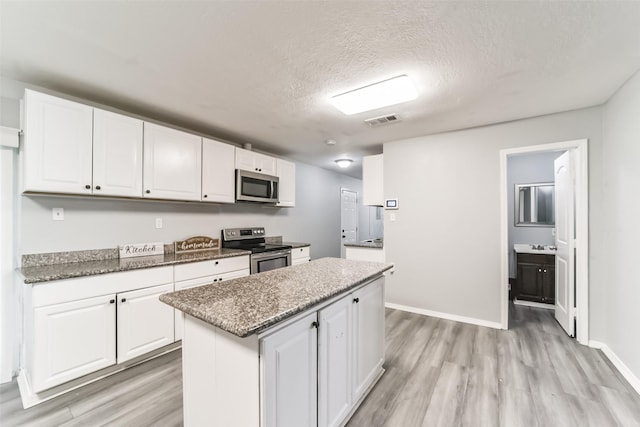 kitchen with light wood finished floors, visible vents, a center island, stainless steel appliances, and white cabinetry