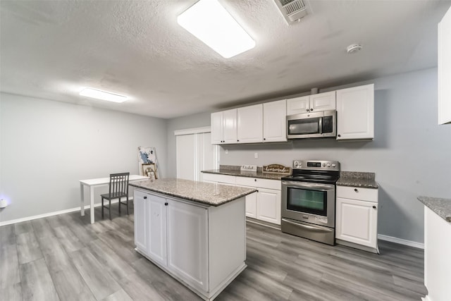 kitchen with visible vents, a kitchen island, stainless steel appliances, light wood-style floors, and white cabinetry