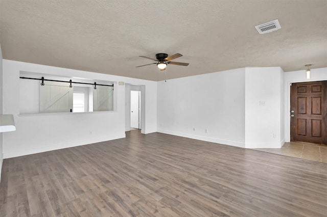 unfurnished living room featuring ceiling fan, a barn door, wood-type flooring, and a textured ceiling