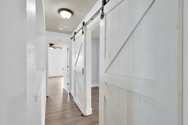 hallway with a textured ceiling, a barn door, and hardwood / wood-style floors