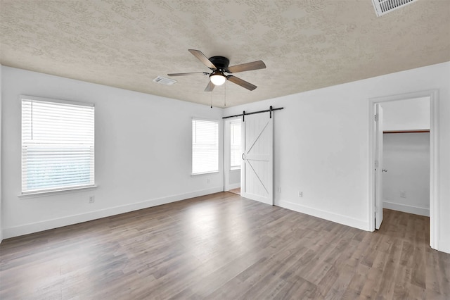 unfurnished bedroom featuring a walk in closet, wood-type flooring, a barn door, and ceiling fan