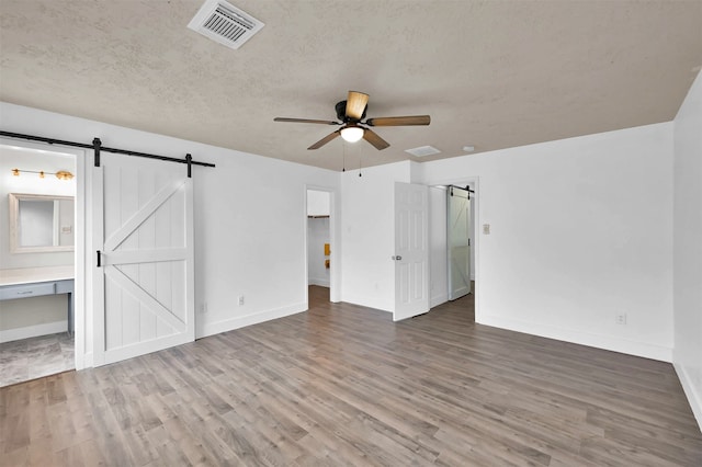 unfurnished room featuring a textured ceiling, ceiling fan, hardwood / wood-style floors, and a barn door