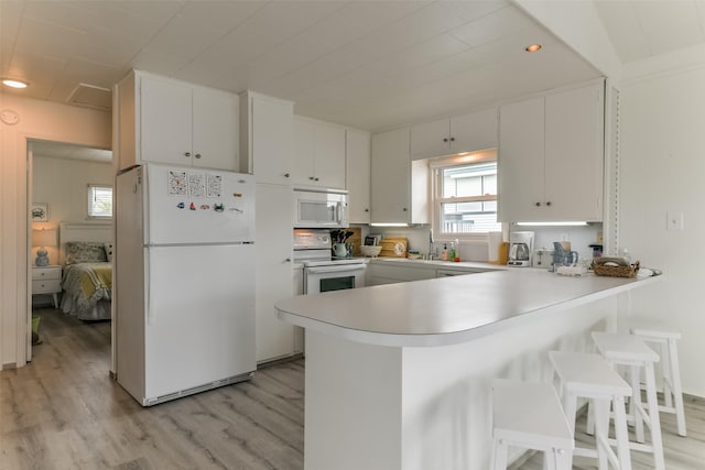 kitchen featuring a wealth of natural light, light countertops, light wood-style flooring, white appliances, and a peninsula