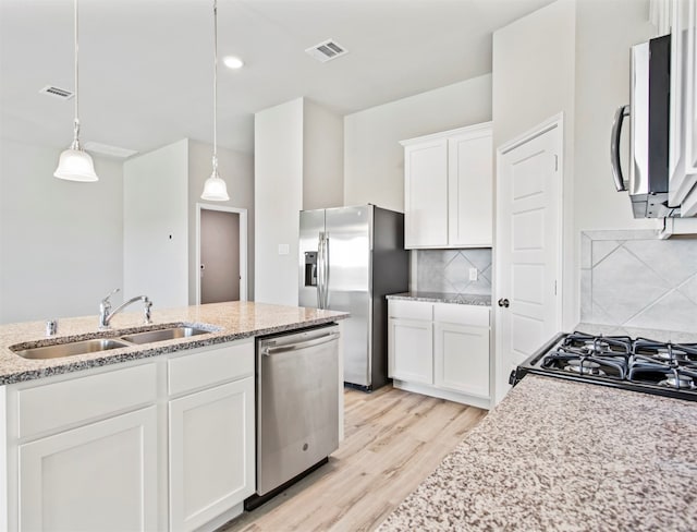 kitchen with sink, appliances with stainless steel finishes, tasteful backsplash, white cabinetry, and pendant lighting