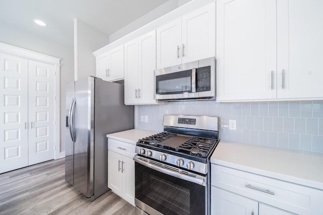 kitchen with appliances with stainless steel finishes, light hardwood / wood-style floors, white cabinetry, and tasteful backsplash