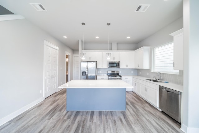 kitchen with white cabinets, light wood-type flooring, appliances with stainless steel finishes, and a kitchen island