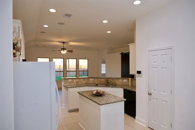 kitchen with a kitchen island, stone counters, white fridge, and white cabinets