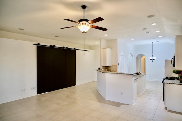 kitchen with white cabinets, dark stone counters, a barn door, and decorative light fixtures