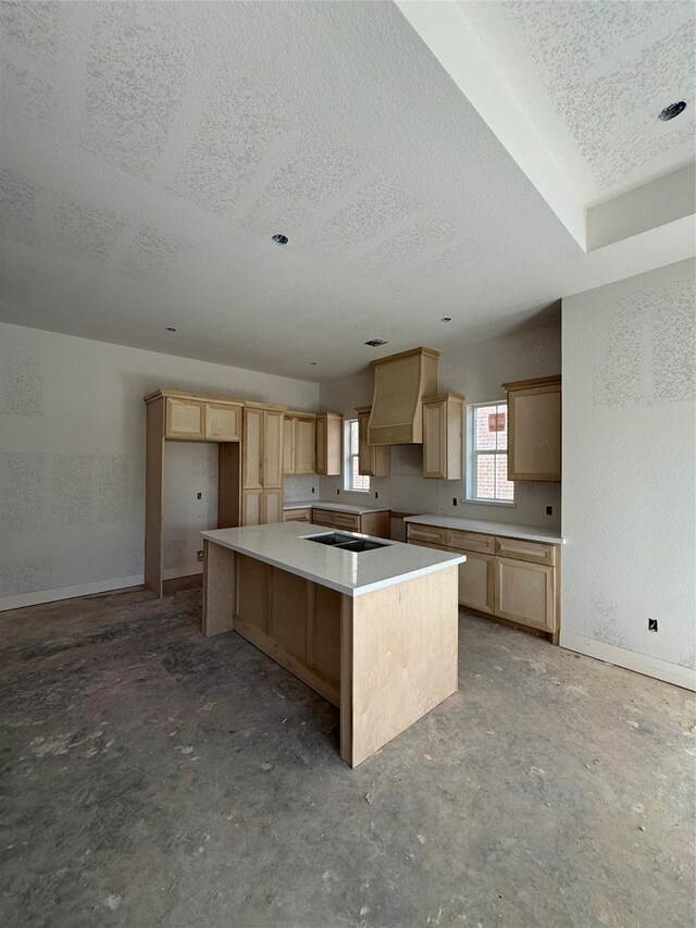 kitchen with concrete flooring, premium range hood, a kitchen island, stovetop, and light brown cabinets