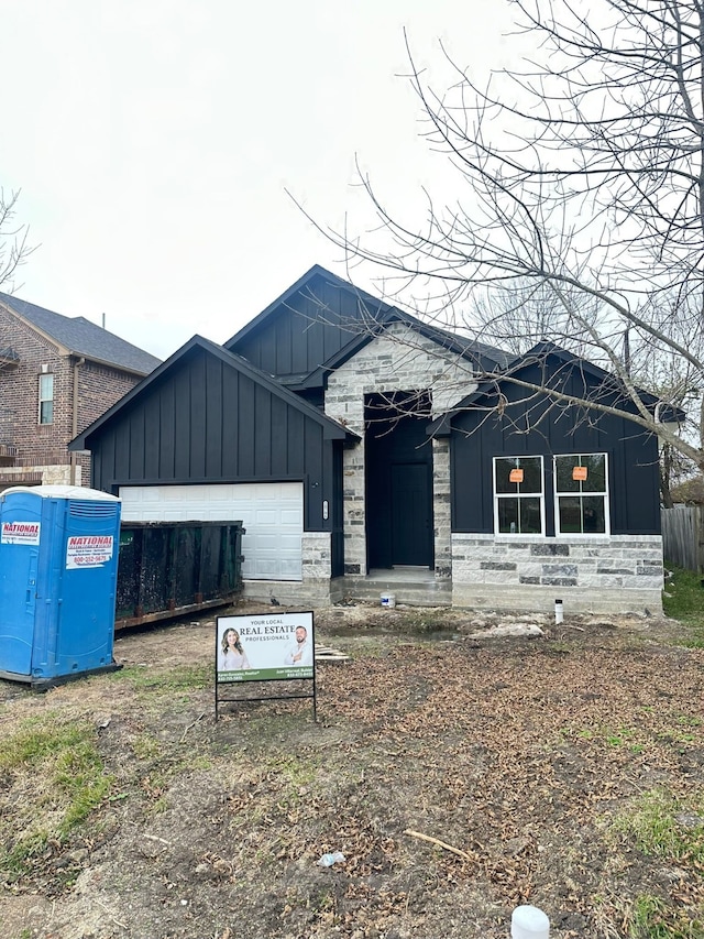 view of front facade with stone siding, board and batten siding, an attached garage, and fence