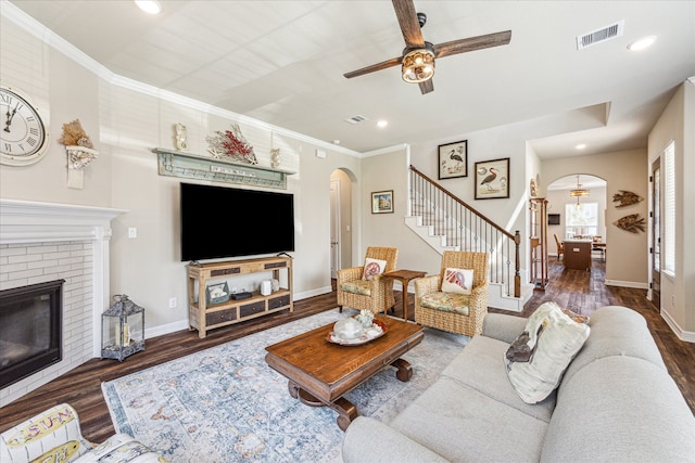 living room featuring ceiling fan, dark hardwood / wood-style flooring, crown molding, and a brick fireplace