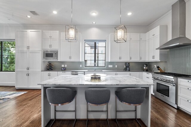 kitchen featuring white cabinetry, appliances with stainless steel finishes, wall chimney exhaust hood, and a center island