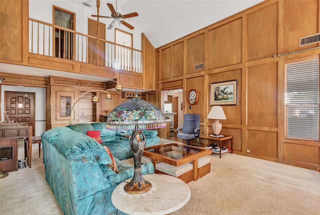 living room with ceiling fan, wooden walls, light carpet, and a high ceiling