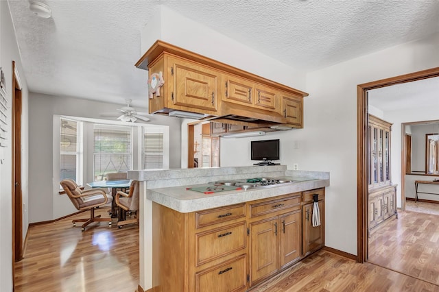 kitchen with stainless steel gas cooktop, kitchen peninsula, light hardwood / wood-style floors, and a textured ceiling