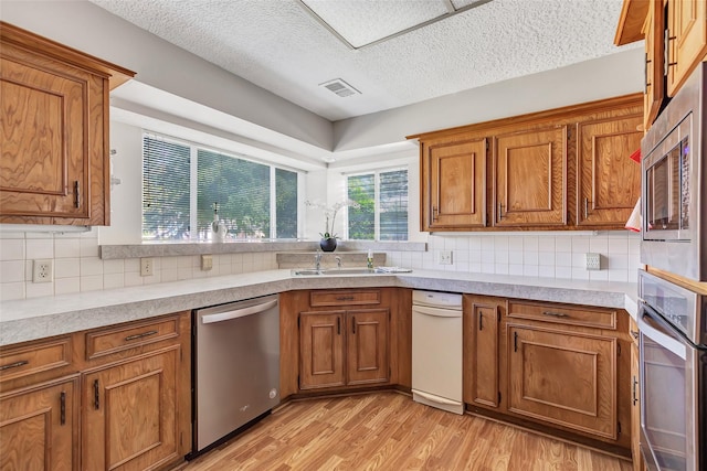 kitchen with sink, a textured ceiling, light wood-type flooring, stainless steel appliances, and decorative backsplash