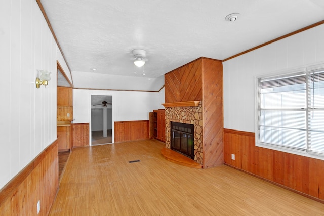 unfurnished living room featuring wood walls, a ceiling fan, wood finished floors, and a stone fireplace