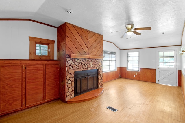 living area featuring lofted ceiling, a textured ceiling, light wood-style flooring, a fireplace, and wainscoting