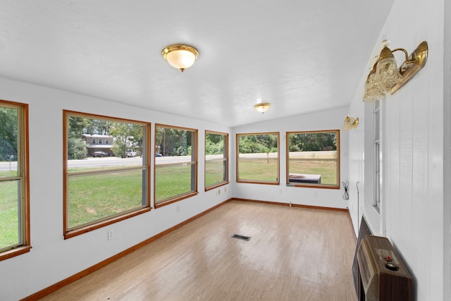 unfurnished sunroom with heating unit, plenty of natural light, visible vents, and vaulted ceiling