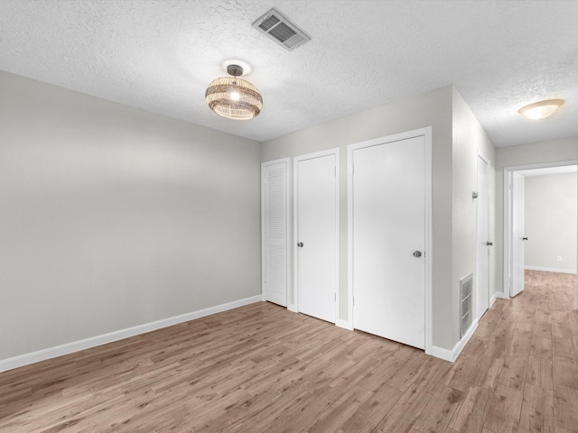 unfurnished bedroom featuring two closets, wood-type flooring, and a textured ceiling