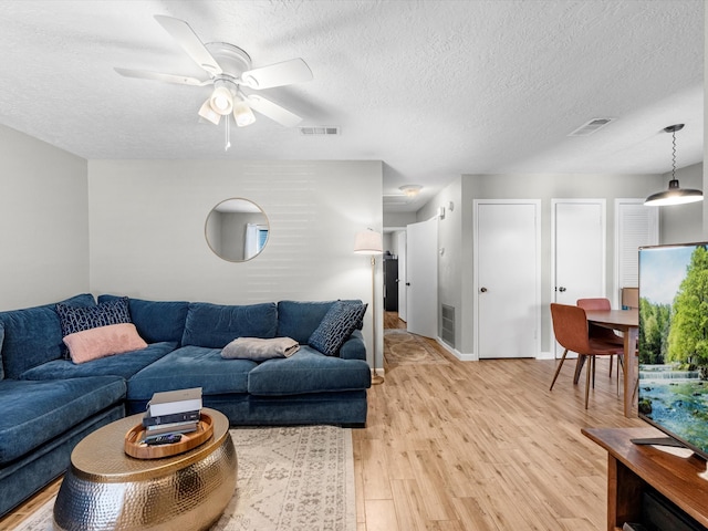 living room featuring ceiling fan, a textured ceiling, and light hardwood / wood-style flooring