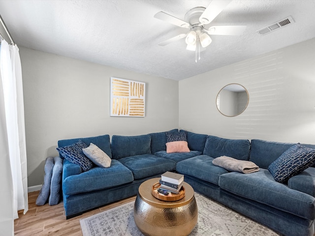 living room featuring ceiling fan, light hardwood / wood-style flooring, and a textured ceiling