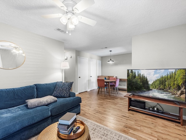 living room featuring a textured ceiling, ceiling fan, and light wood-type flooring