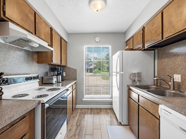 kitchen featuring sink, white appliances, light hardwood / wood-style floors, tasteful backsplash, and a textured ceiling