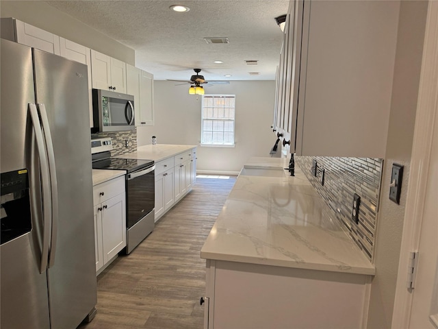 kitchen featuring light stone countertops, appliances with stainless steel finishes, sink, light hardwood / wood-style flooring, and white cabinetry