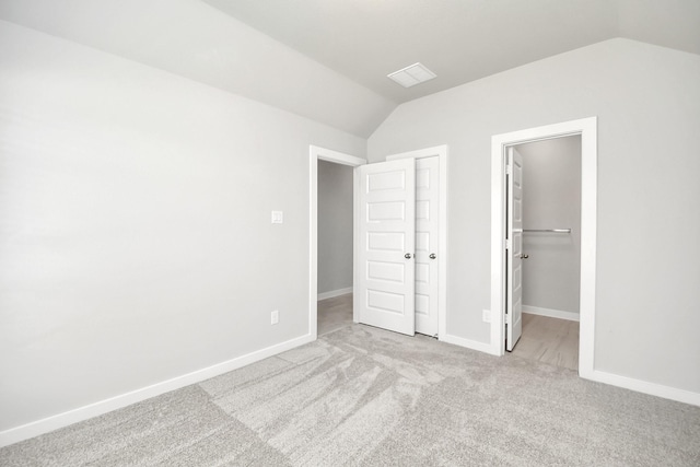 unfurnished bedroom featuring a walk in closet, light carpet, and lofted ceiling