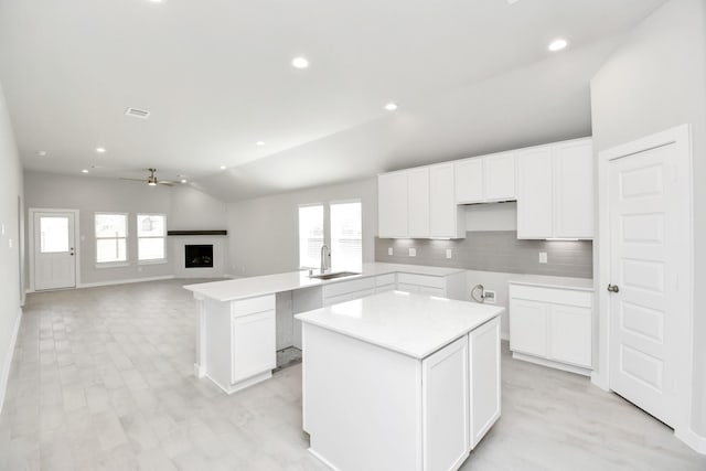 kitchen with lofted ceiling, white cabinets, ceiling fan, a kitchen island, and kitchen peninsula