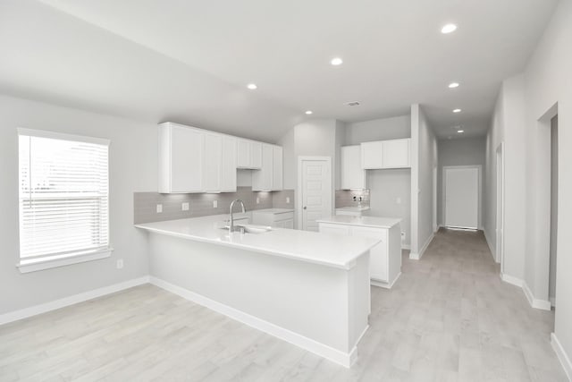 kitchen featuring kitchen peninsula, decorative backsplash, sink, light hardwood / wood-style flooring, and white cabinetry