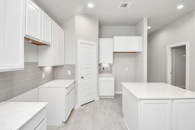 kitchen with a center island, white cabinets, decorative backsplash, light hardwood / wood-style floors, and light stone counters