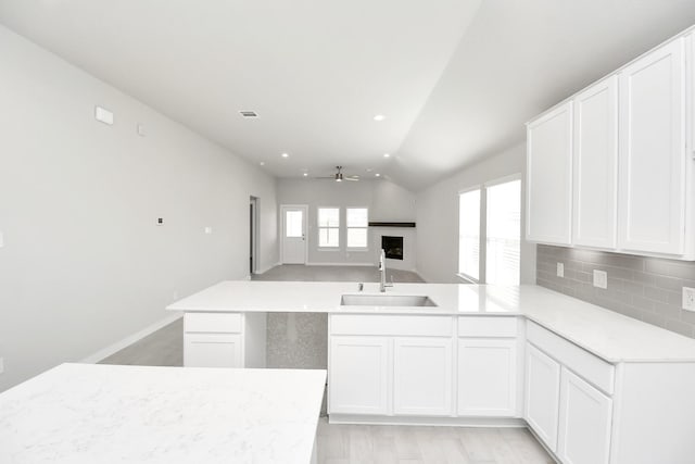 kitchen featuring kitchen peninsula, tasteful backsplash, ceiling fan, sink, and white cabinetry