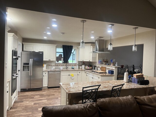 kitchen with stainless steel appliances, light hardwood / wood-style flooring, sink, light stone counters, and wall chimney range hood