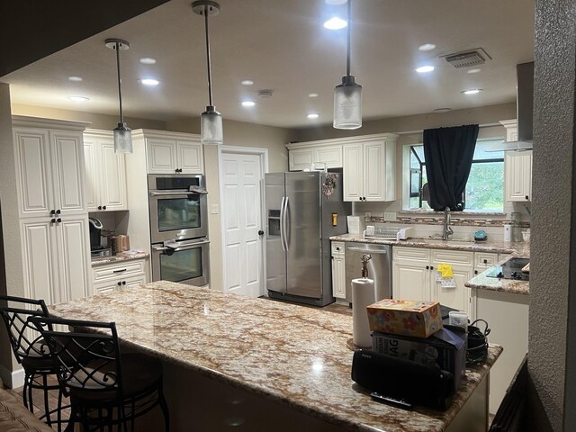 kitchen with appliances with stainless steel finishes, light stone counters, white cabinetry, and decorative light fixtures