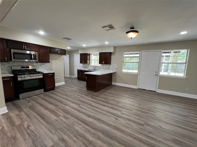 kitchen featuring hardwood / wood-style floors, sink, appliances with stainless steel finishes, tasteful backsplash, and kitchen peninsula