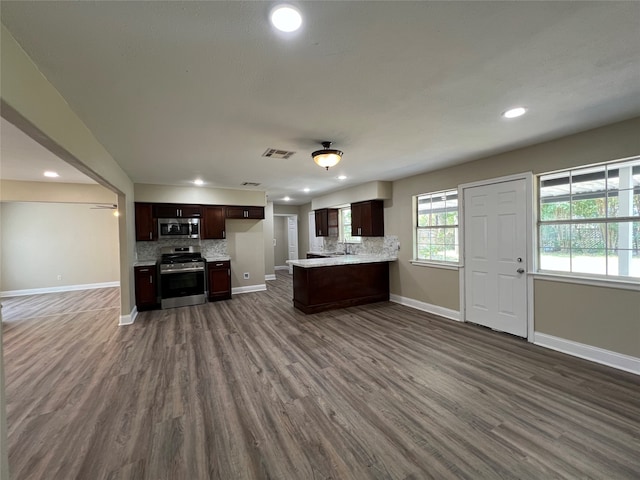 kitchen with dark hardwood / wood-style flooring, appliances with stainless steel finishes, dark brown cabinets, decorative backsplash, and kitchen peninsula